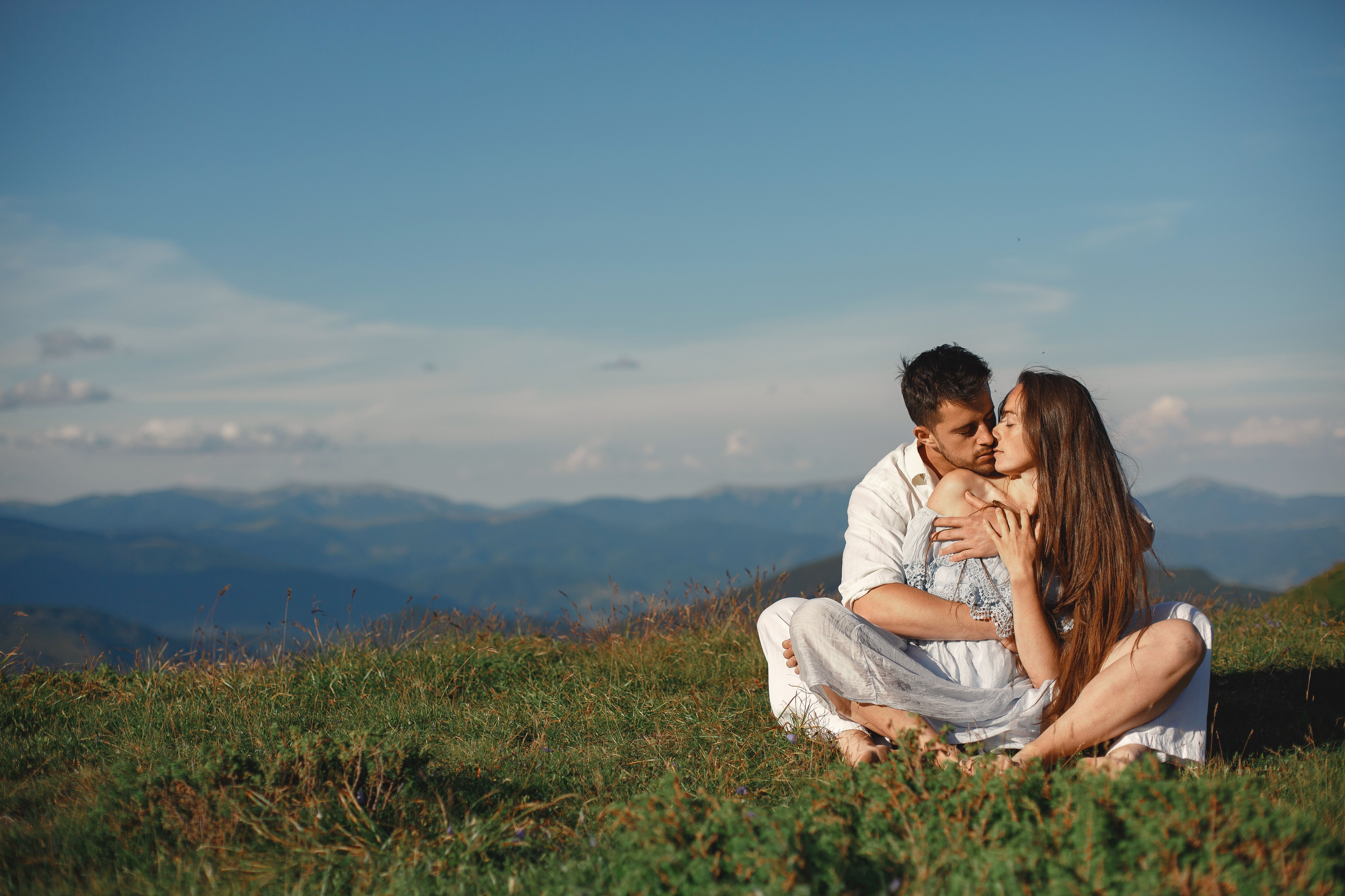 A couple sitting together on a grassy hilltop with a scenic mountain view, showcasing love and serenity.