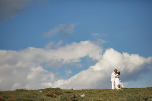 Free Couple Kissing while Standing on Green Grass Field Under White Clouds and Blue Sky Stock Photo