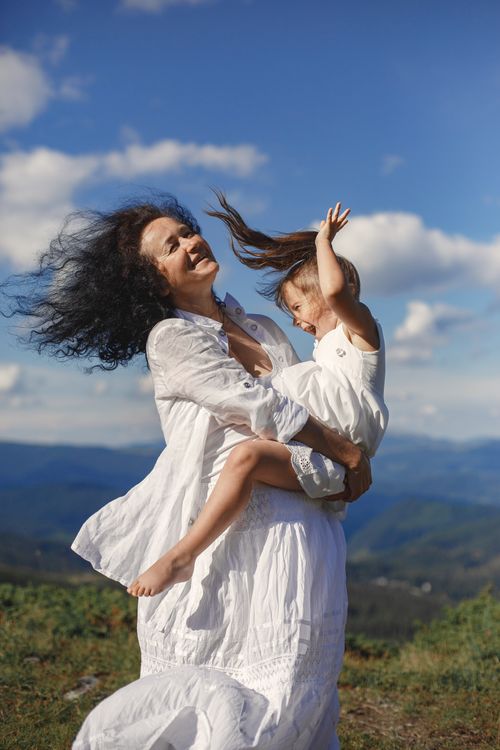 Free Mother and daughter enjoying a playful moment in nature against a vibrant blue sky backdrop. Stock Photo