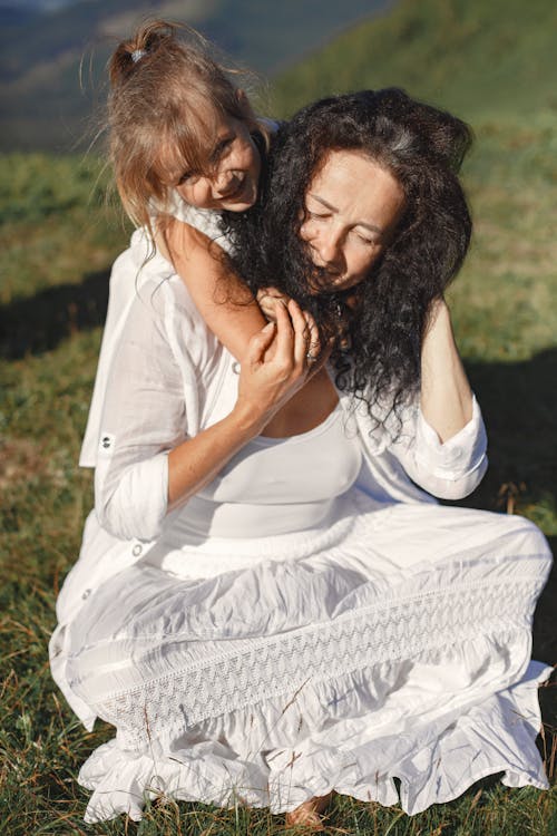 A Girl Hugging a Woman While Sitting on the Grass