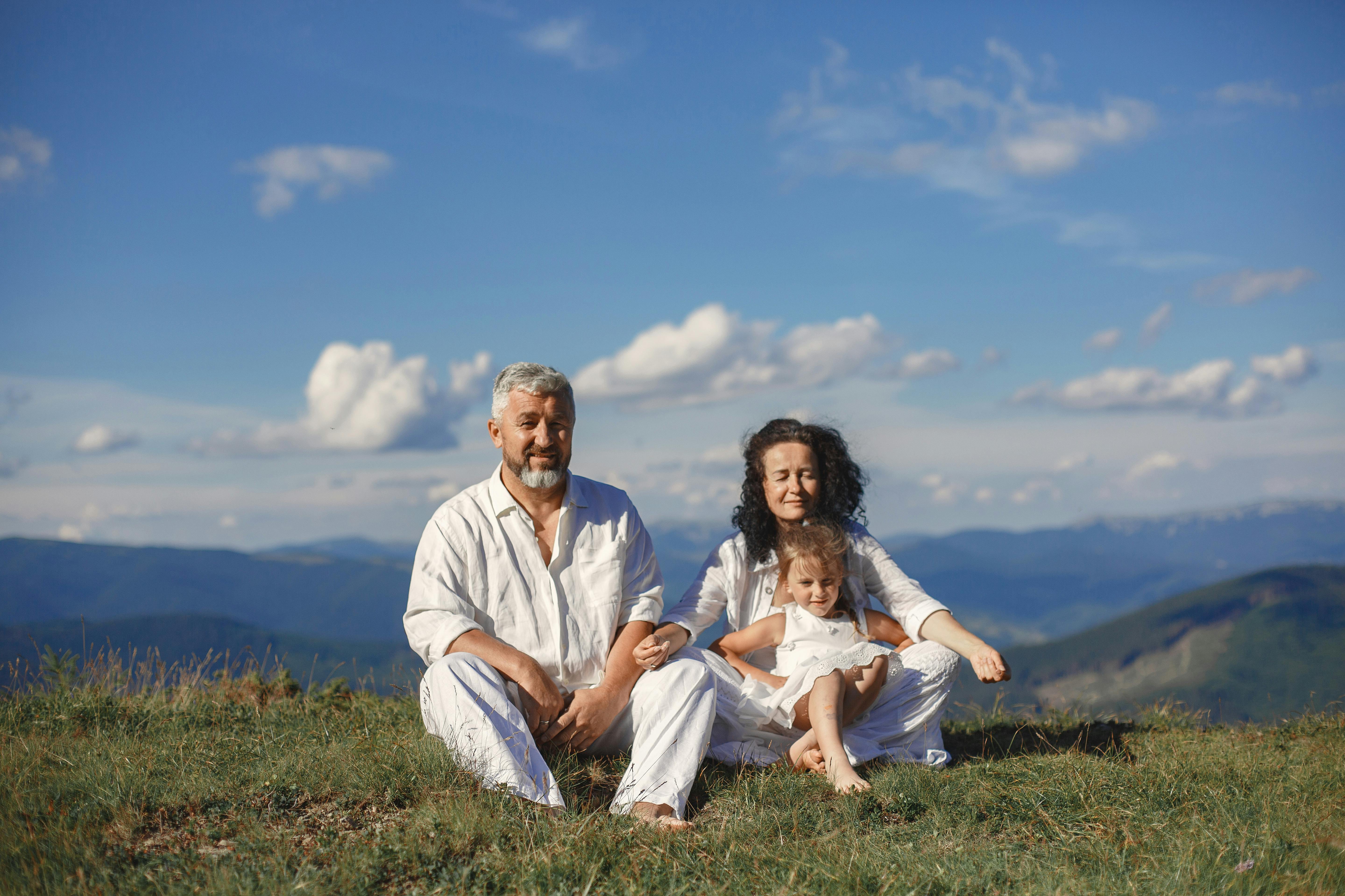 A happy family enjoys a sunny day outdoors, sitting together on a grass field.