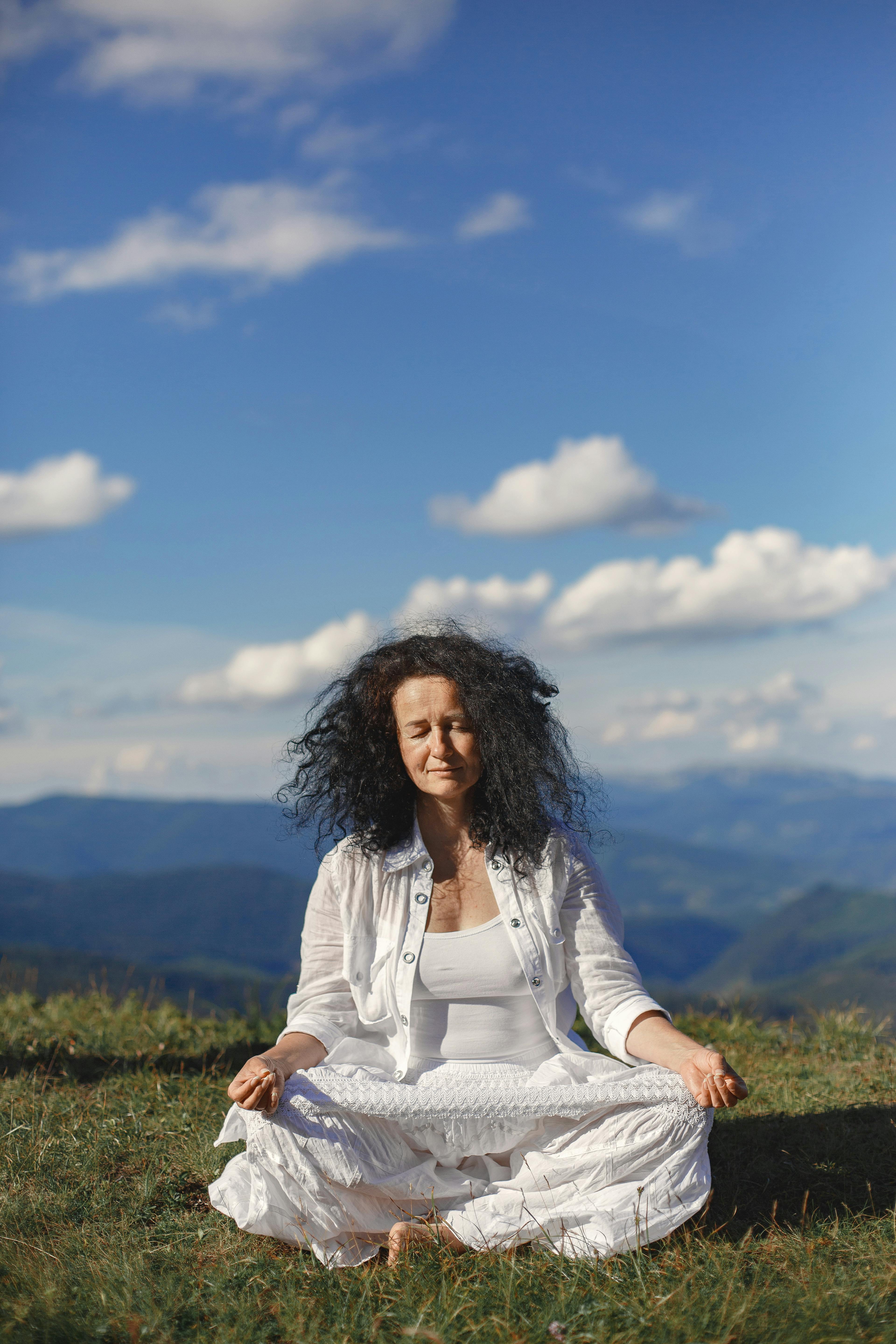 Woman meditating in peaceful mountain scenery under a bright blue sky.