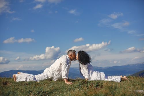 Free Couple kissing in yoga pose on a grassy hill under a clear blue sky. Stock Photo