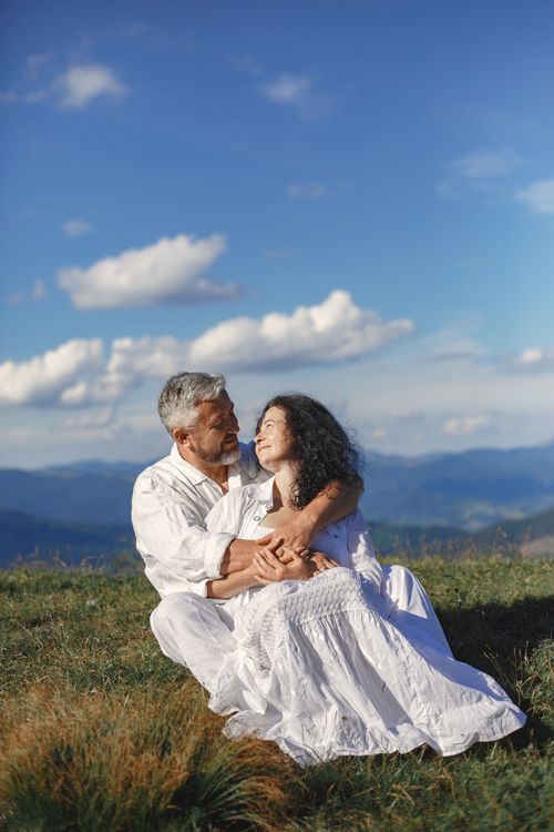 Free A loving couple sitting together outdoors on a sunny hilltop, embracing under a clear blue sky. Stock Photo