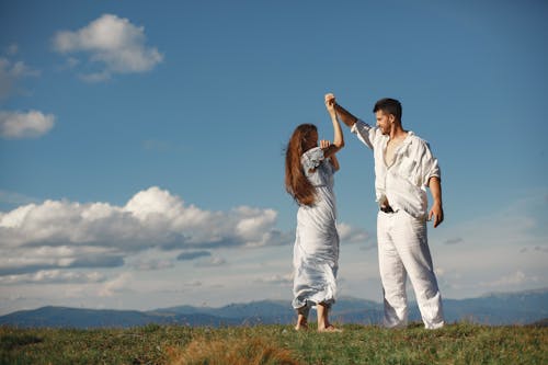 Man and Woman Standing on Green Grass Field Under Blue Sky