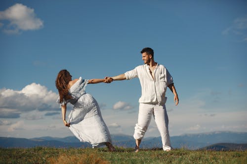Man and Woman Holding Hands While Dancing on Green Grass Field