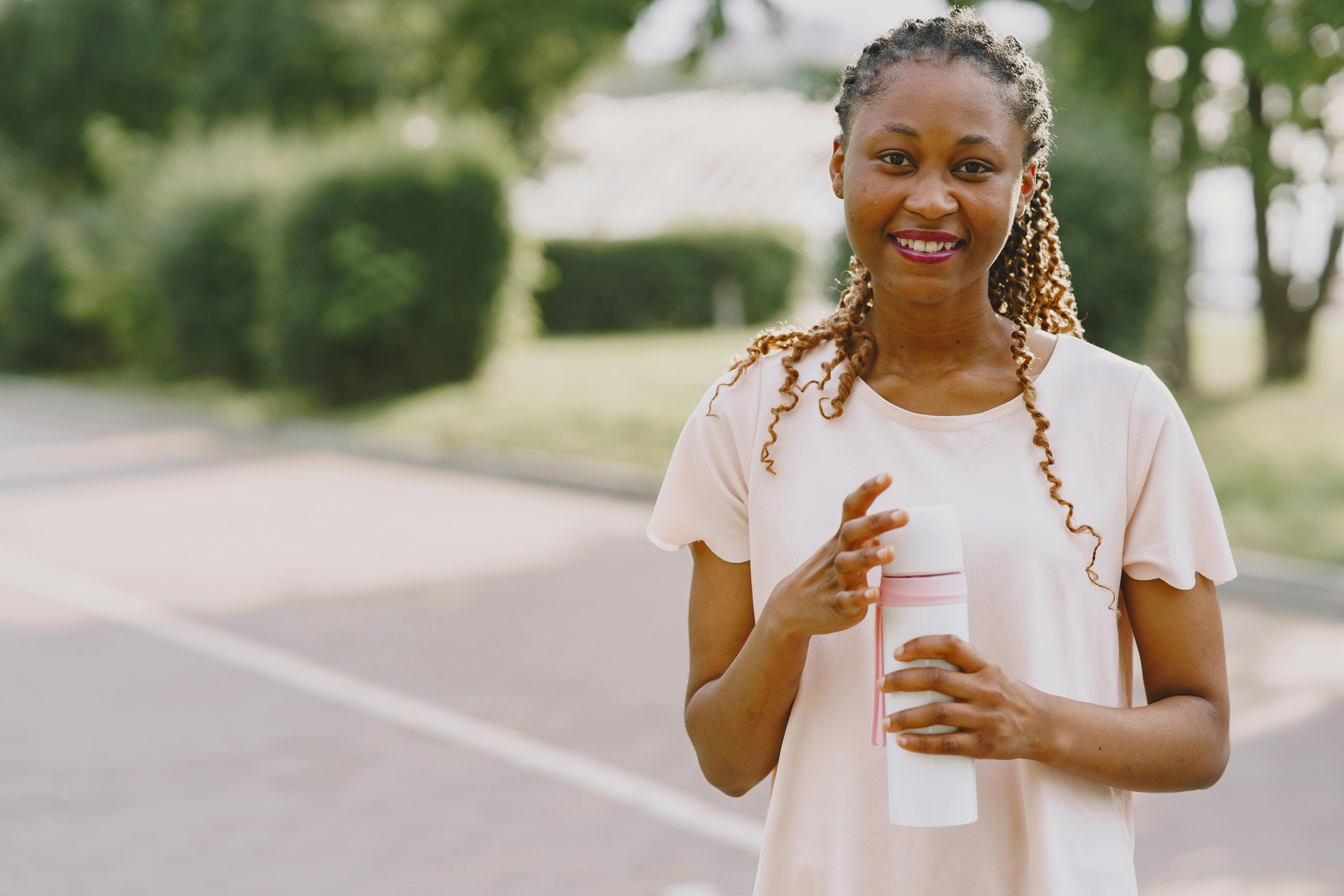 Happy woman enjoying a sunny day with her tumbler in a park setting.