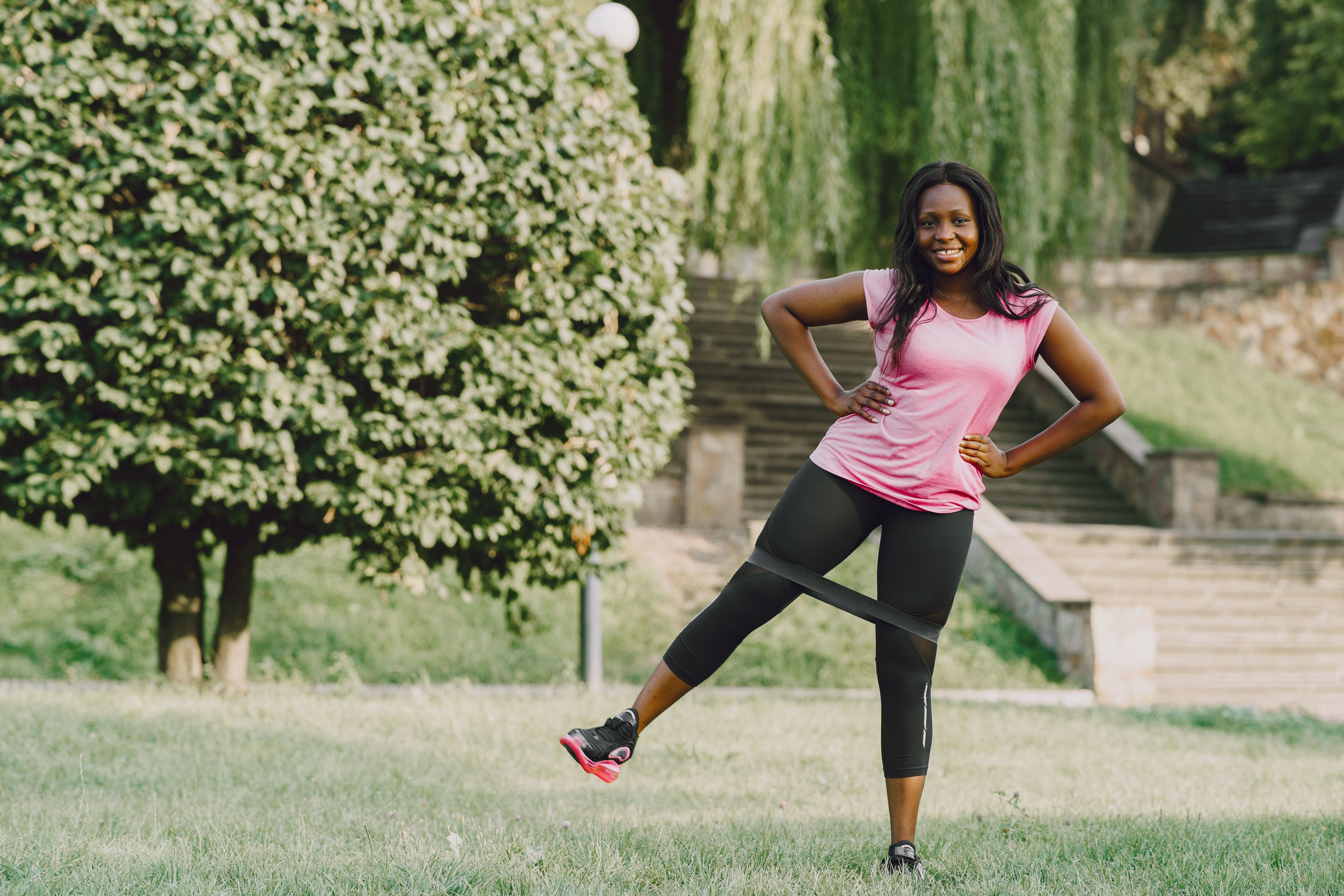 Woman in Pink Tank Top and Black Leggings Sitting on Green Grass Field