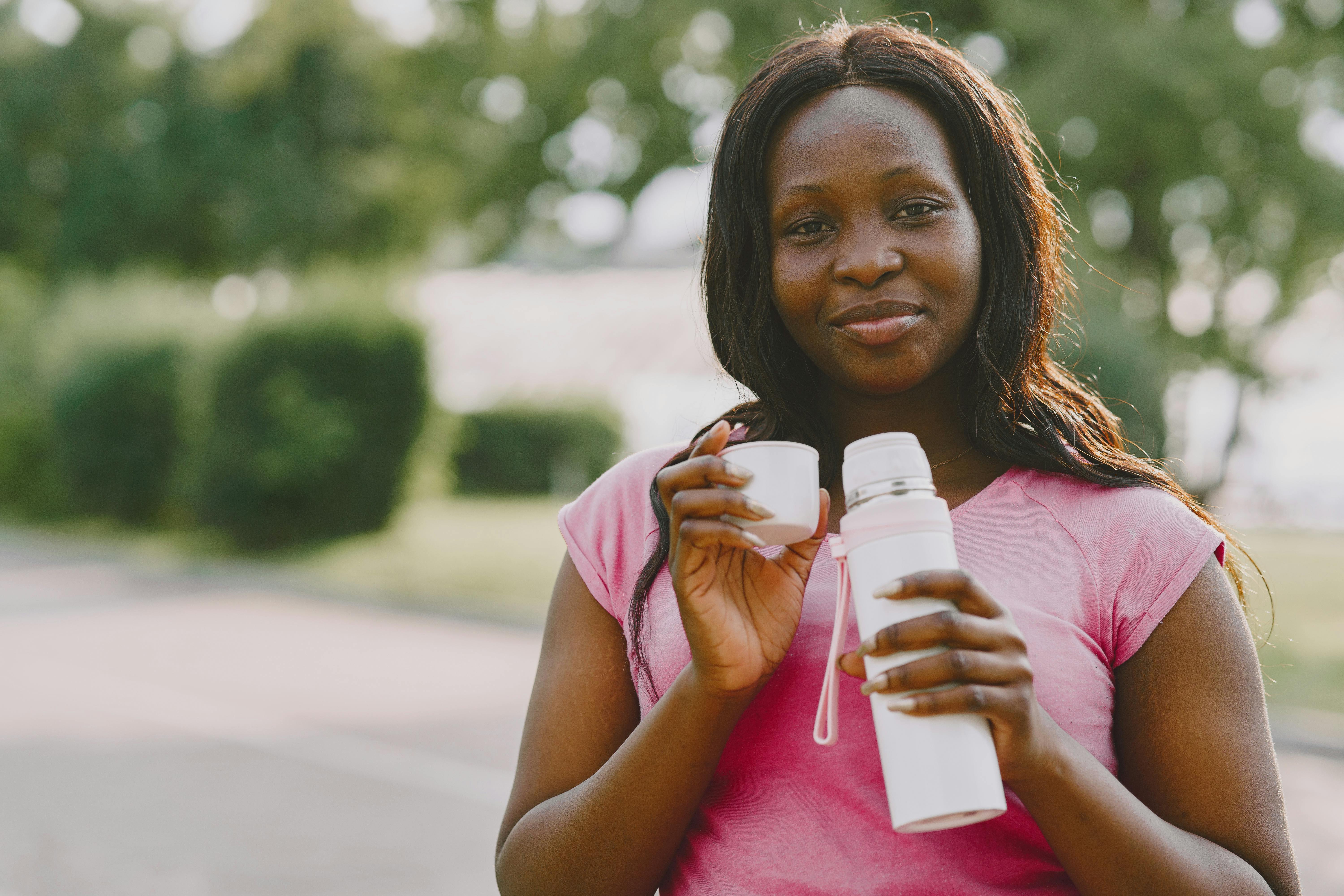 African American woman enjoying a warm drink outdoors in a park setting.