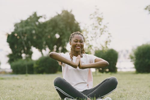 Free Woman in White Shirt and Gray Leggings Sitting on Green Grass Field Stock Photo