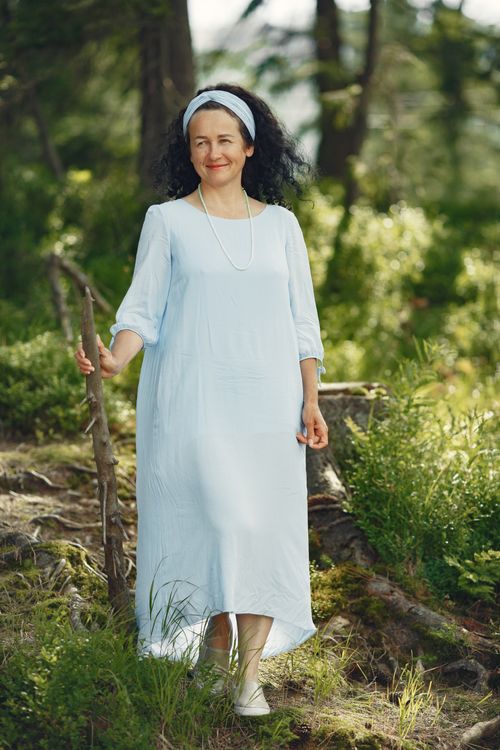 Free Smiling woman in blue dress walking with a stick in a green forest. Stock Photo