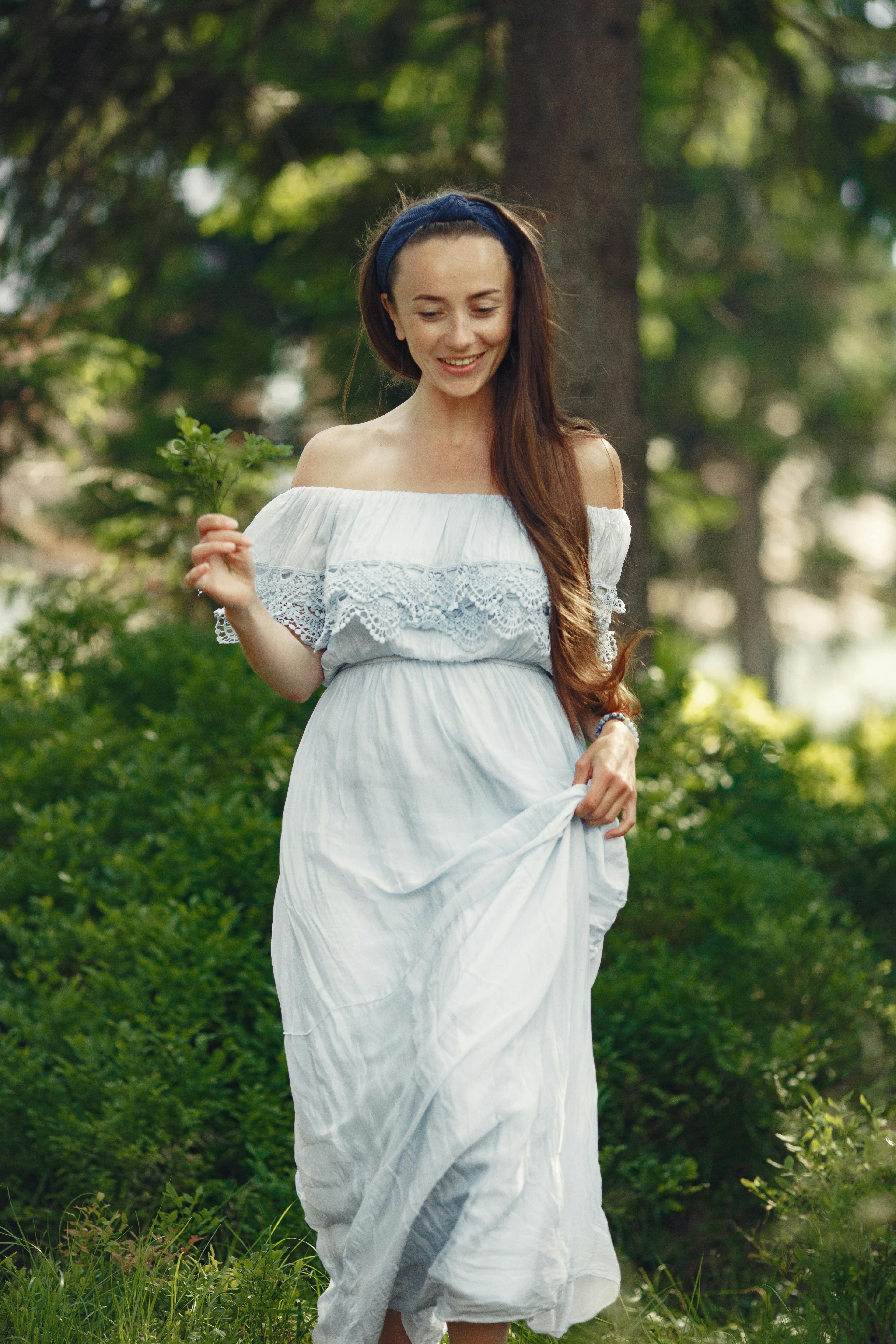 阳光明媚的日子里，一个穿着白色蕾丝连衣裙的女人微笑着走过郁郁葱葱的绿叶