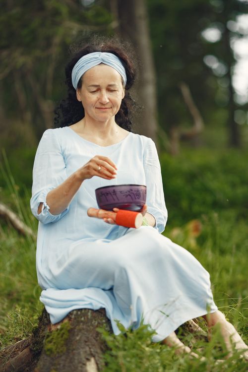 Free A woman meditates in a forest setting, using a Tibetan singing bowl for relaxation. Stock Photo