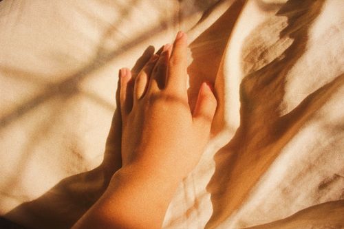 Free A hand rests on a sunlit fabric, casting a warm shadow, evoking a cozy and calm atmosphere. Stock Photo