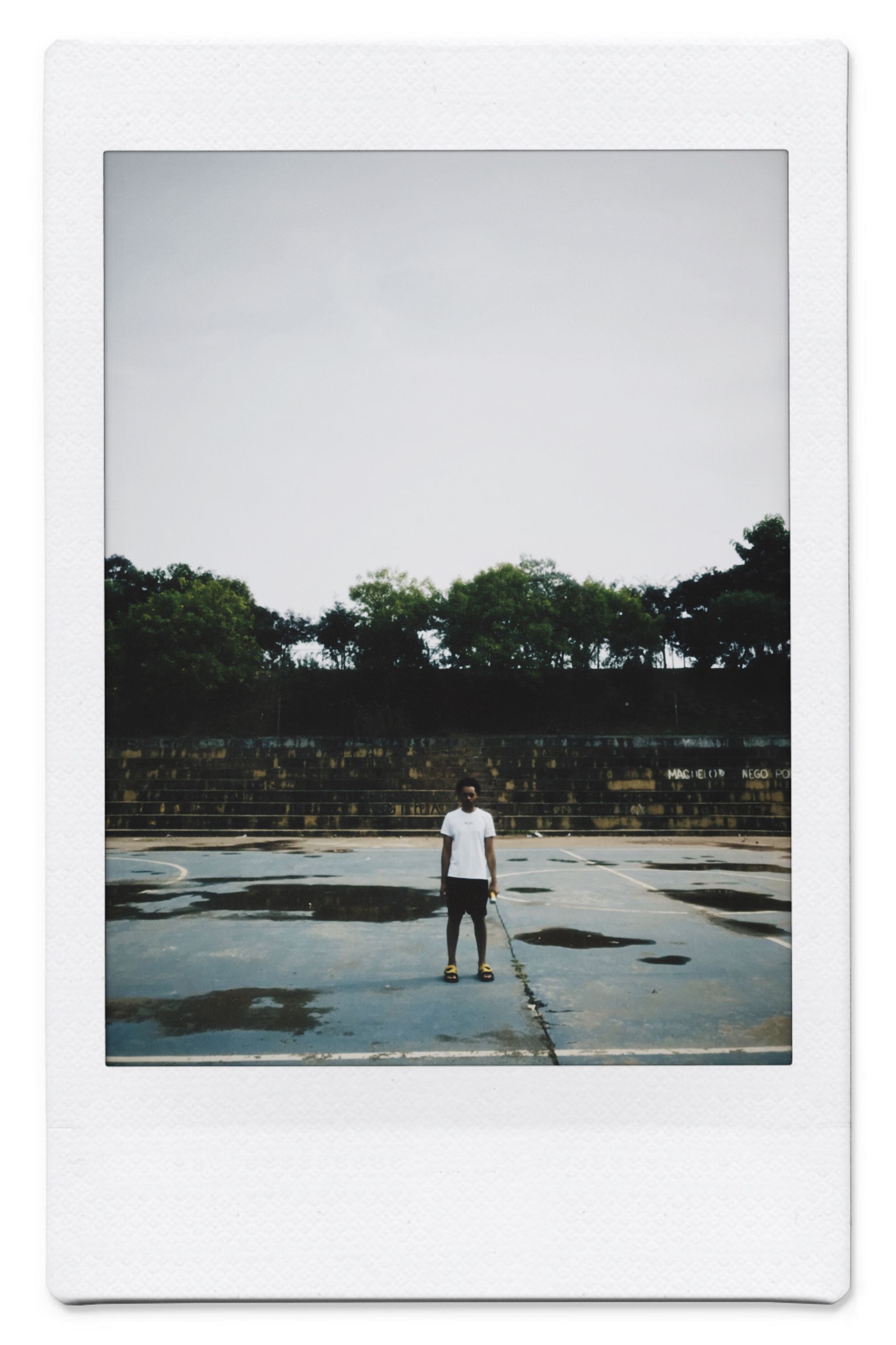 A lone man standing on concrete pavement in a park, captured in polaroid style.