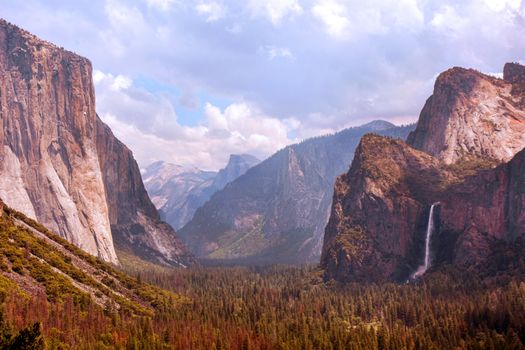 Vibrant landscape of Yosemite Valley featuring iconic cliffs and waterfalls under a cloudy sky.