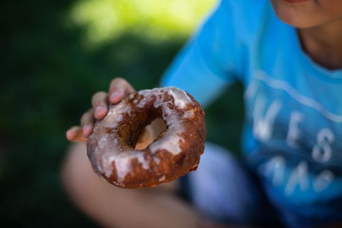 Free A child holding a delicious glazed donut with a blurred green background, perfect for food photography. Stock Photo