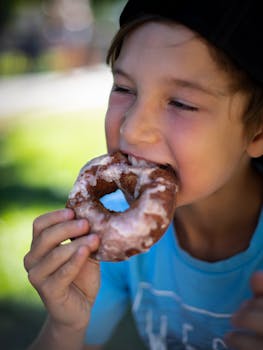 A young boy bites into a delicious chocolate donut with sugar glaze.