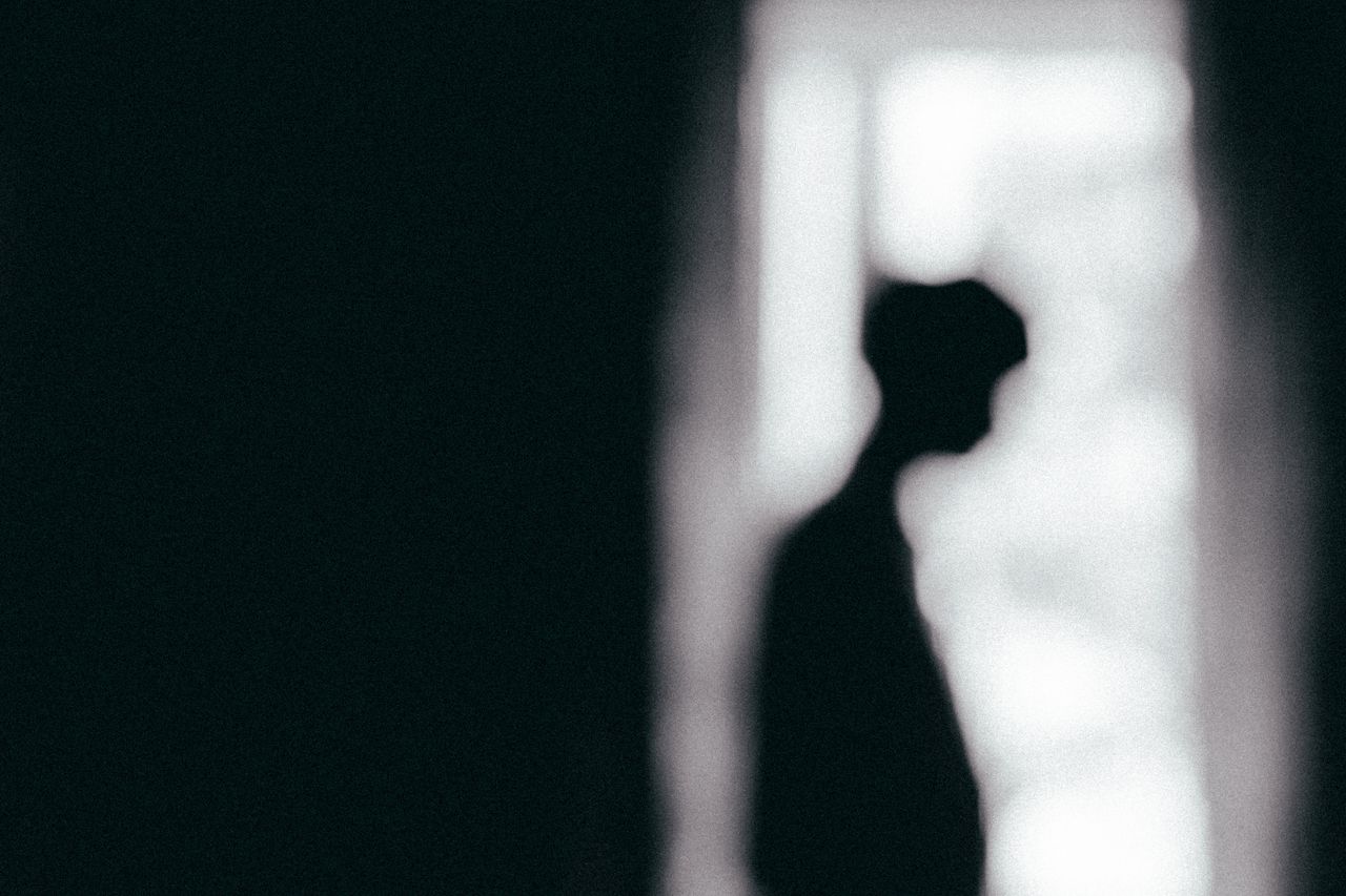 moody black and white silhouette of a person standing by a window conv