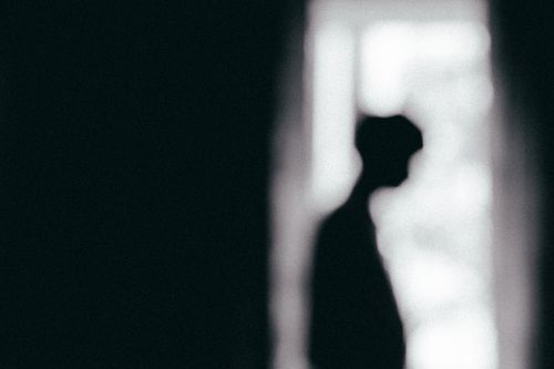Free Moody black and white silhouette of a person standing by a window, conveying solitude. Stock Photo