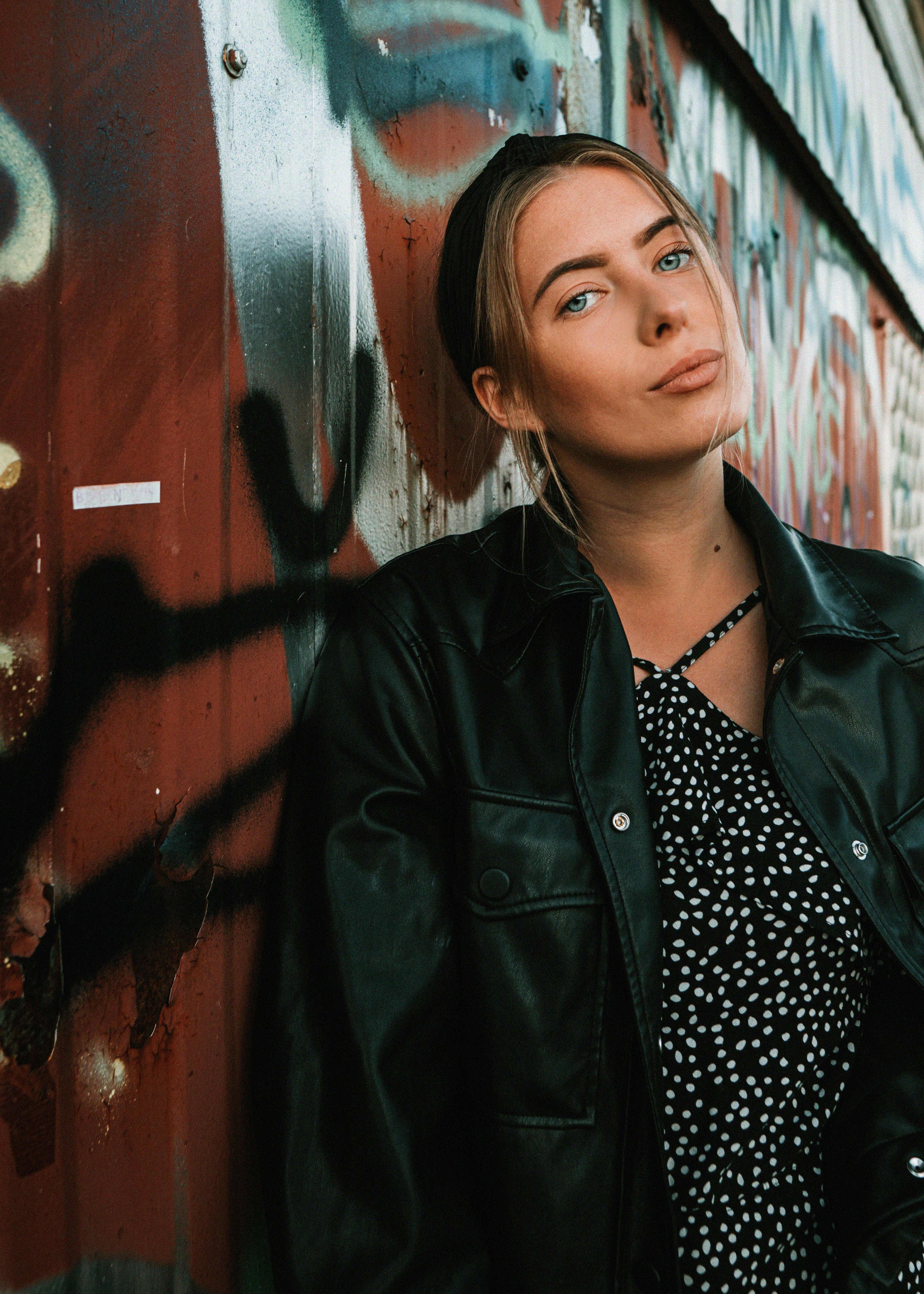 Portrait of a young woman in Lithuania with a graffiti background. Stylish black jacket and vibrant urban setting.