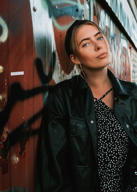 Portrait of a young woman in Lithuania with a graffiti background. Stylish black jacket and vibrant urban setting.