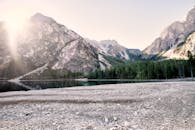 日出映照着宁静的湖泊、树木与高山，构成一幅和平的山景