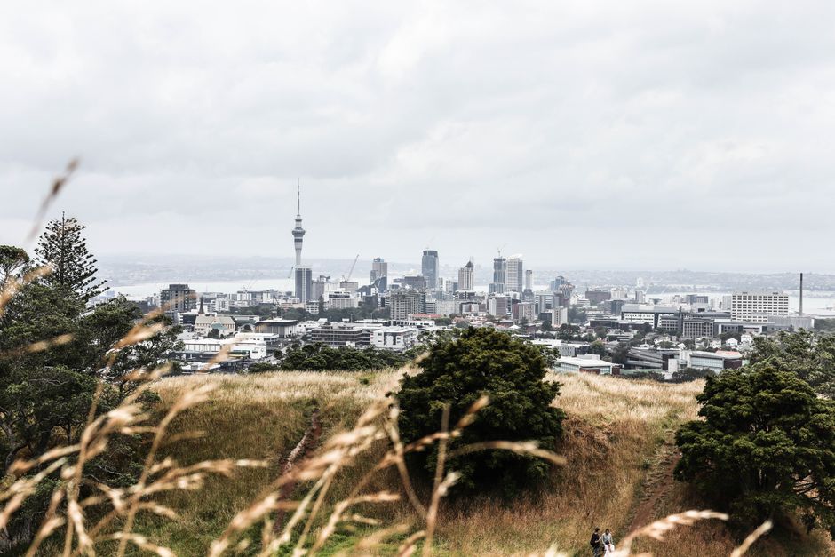 Distant view of Auckland's skyline from Mount Eden with sky tower under cloudy skies.