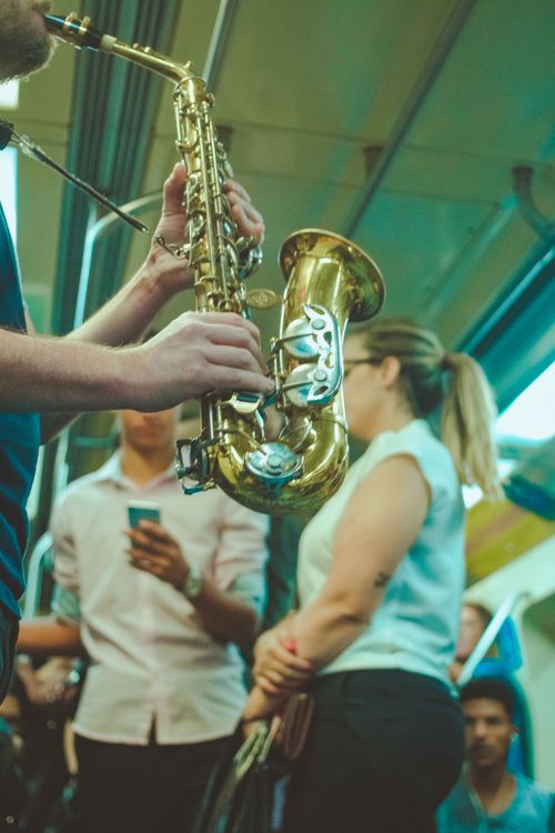 Free Low angle of crop unrecognizable male musician playing saxophone in public transport near passengers Stock Photo