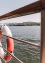 Lifesaver attached to railing of modern boat deck floating on rippling river on sunny summer day