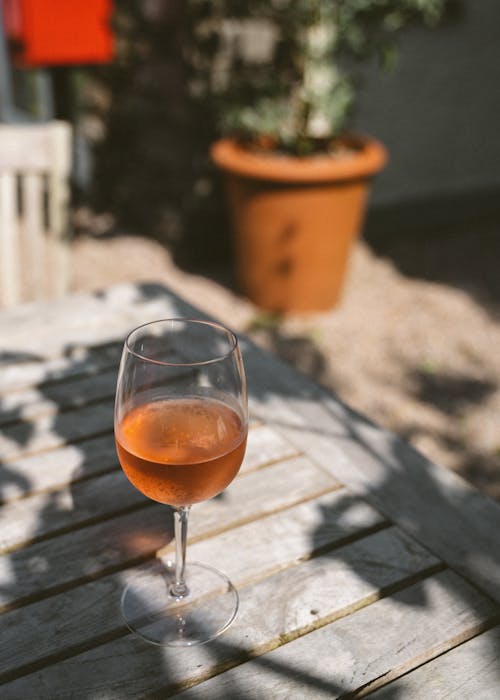 High angle wineglass of refreshing alcoholic beverage placed on wooden square table on sunny terrace