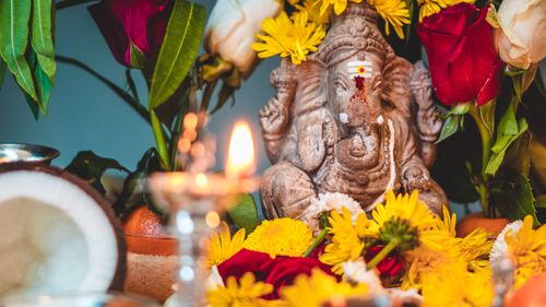 Free Close-up of a Ganesha statue adorned with vibrant flowers and a lit candle, creating a serene atmosphere. Stock Photo