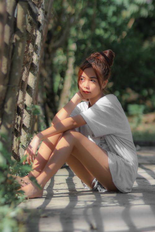 Free Side view full body of peaceful barefoot ethnic female sitting near wooden fence in sunshine Stock Photo