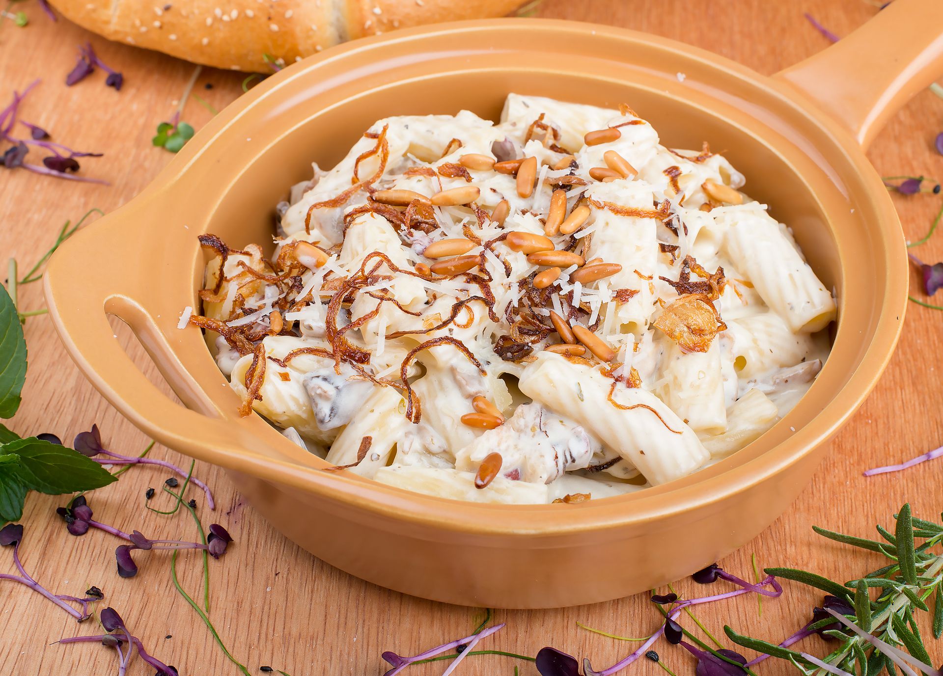 Delicious creamy rigatoni pasta topped with toasted almonds and crispy onions in a ceramic dish.