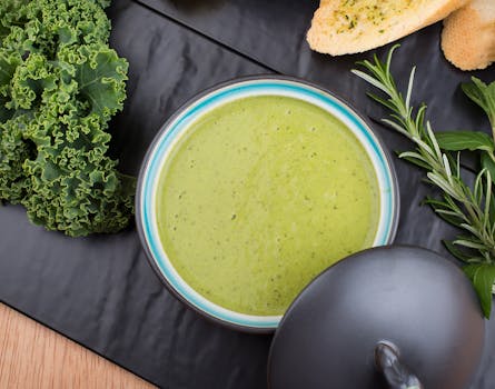 A flavorful green soup garnished with fresh kale and herbs, perfect for a healthy meal.