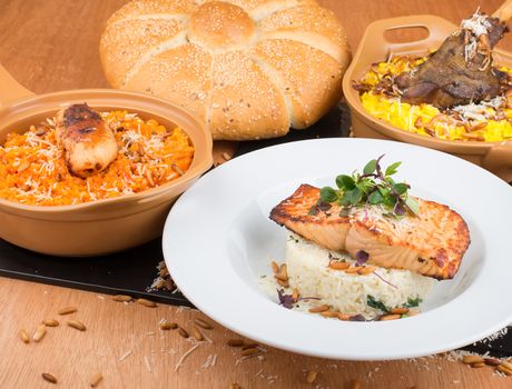 A delicious gourmet meal featuring grilled salmon, rice, and a variety of sides with freshly baked bread.