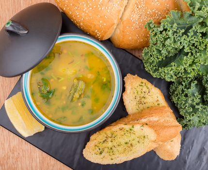 Delicious soup served with garlic bread, kale, and fresh loaf on a table.