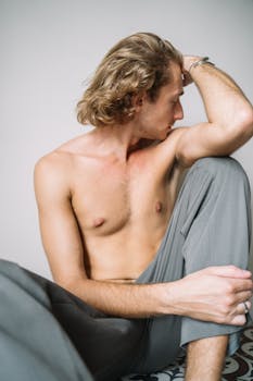 A thoughtful shirtless man sits indoors, showcasing modern portrait photography.