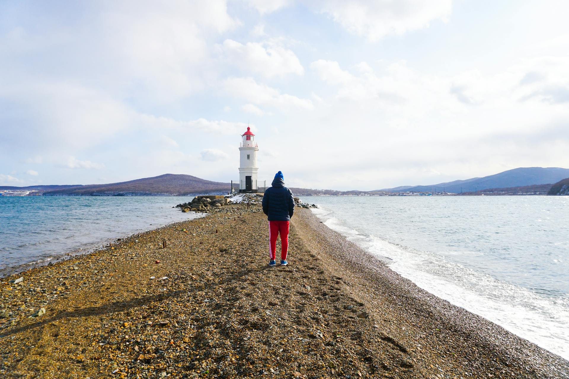 Person walking on a pebble path towards Tokarevsky Lighthouse in Vladivostok, Russia.