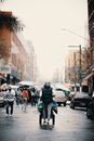 Back view of anonymous person pushing cart while walking on street with cars and pedestrians at daytime