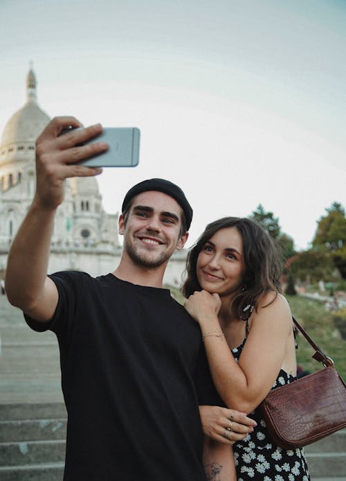 Man in Black Crew Neck Shirt Holding s Smartphone Beside Woman in Black Dress