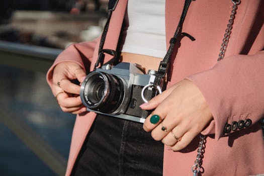 Woman with pink blazer holding a vintage camera outdoors with accessories visible.