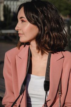 Stylish woman with short hair in a pink blazer enjoying a sunny day outdoors.