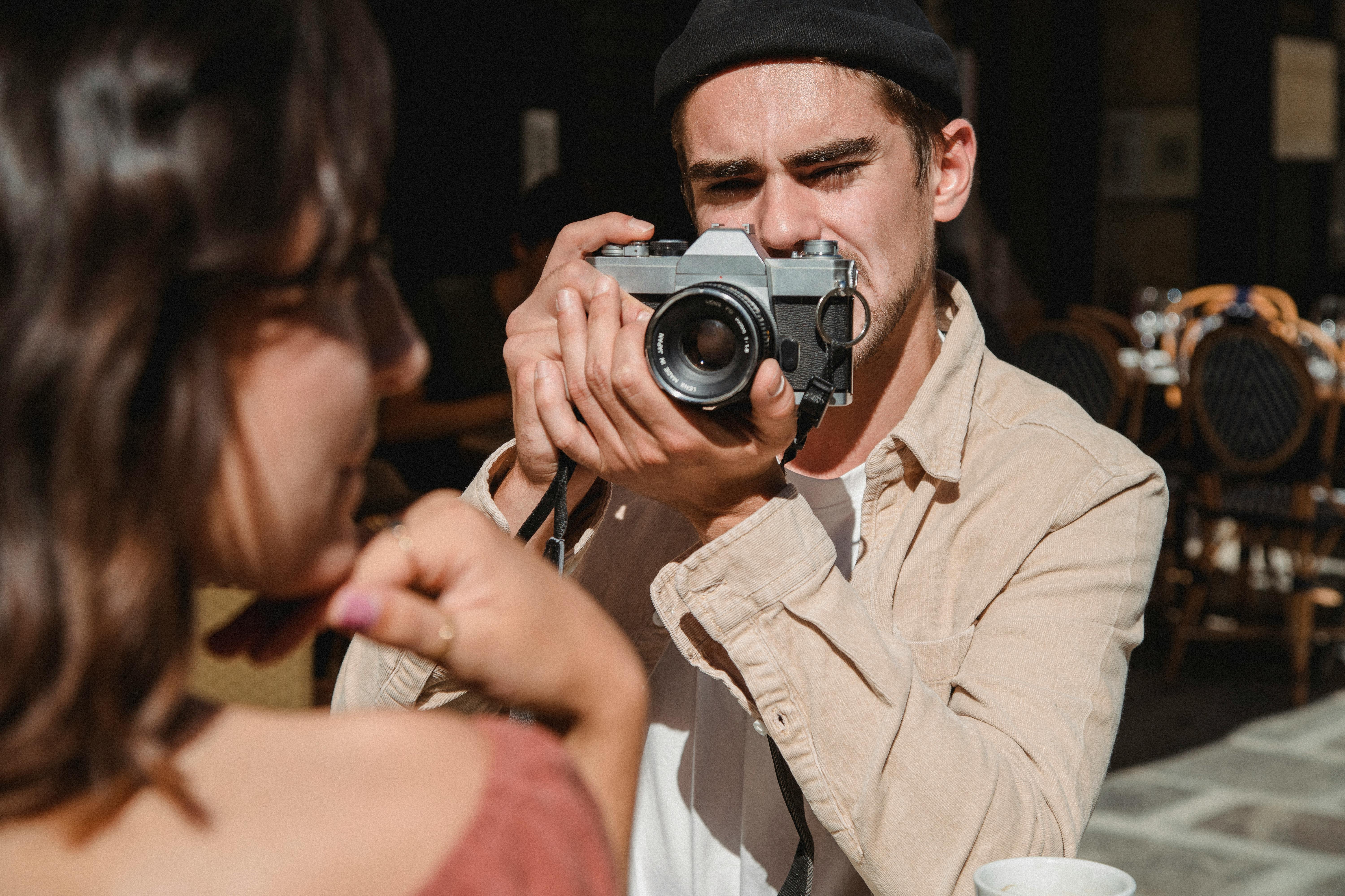 A man taking a photo of a woman with a vintage camera in an outdoor cafe setting.