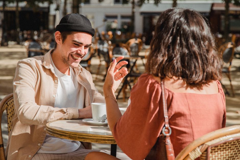 Happy couple enjoying a sunny day at an outdoor cafe, sharing laughter over coffee.