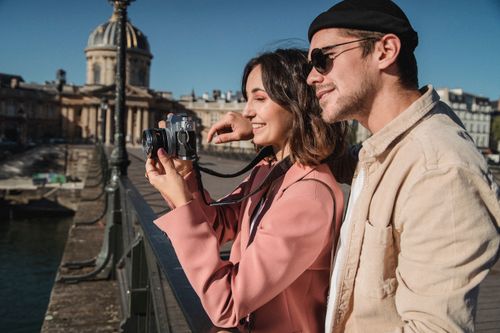 Free Couple enjoying photography on a Parisian bridge, capturing moments together. Stock Photo