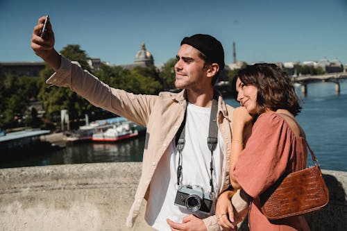 Man in Beige Long Sleeve Shirt Taking a Selfie with a Woman