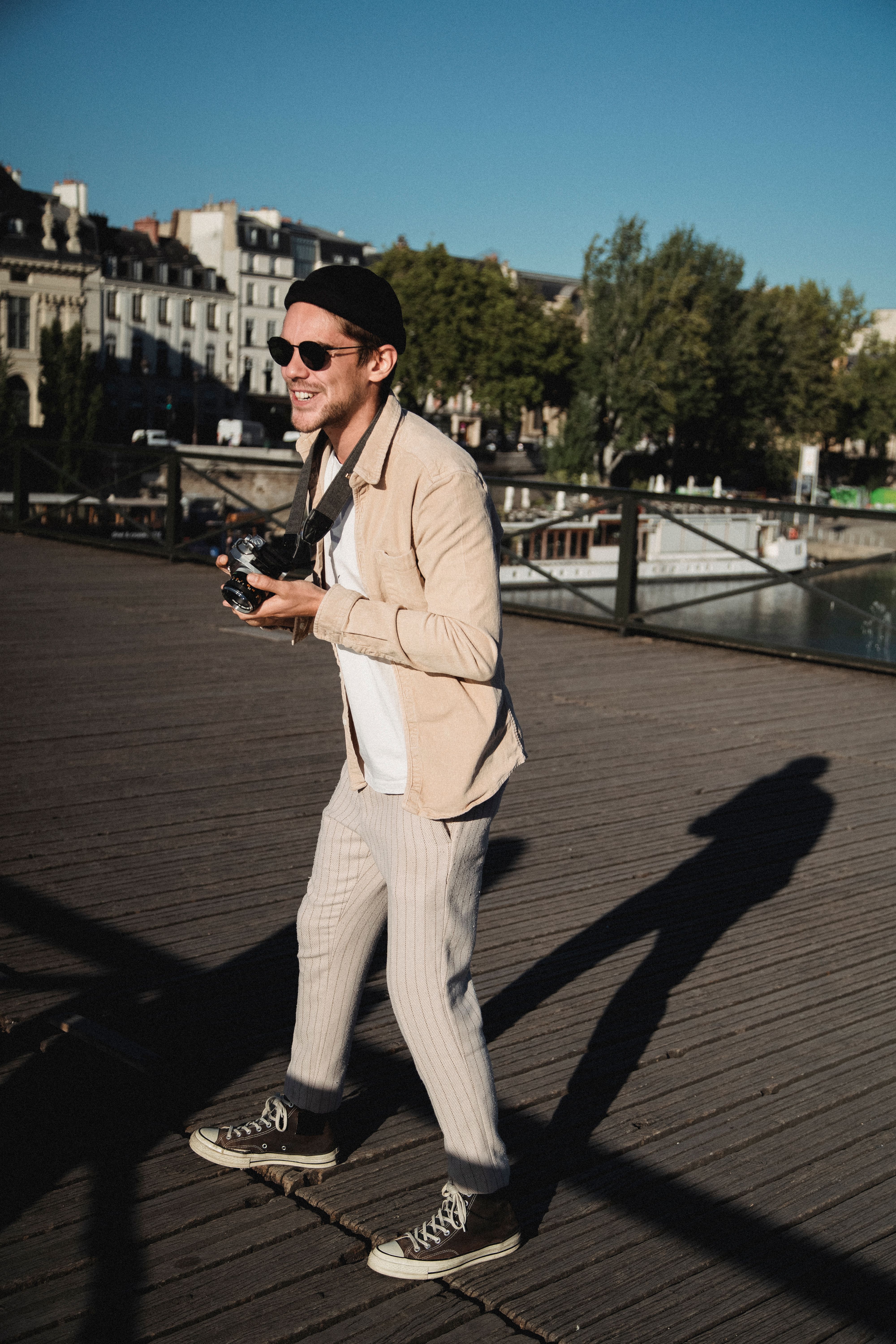 Smiling young man with a camera capturing moments outdoors on a sunny day.