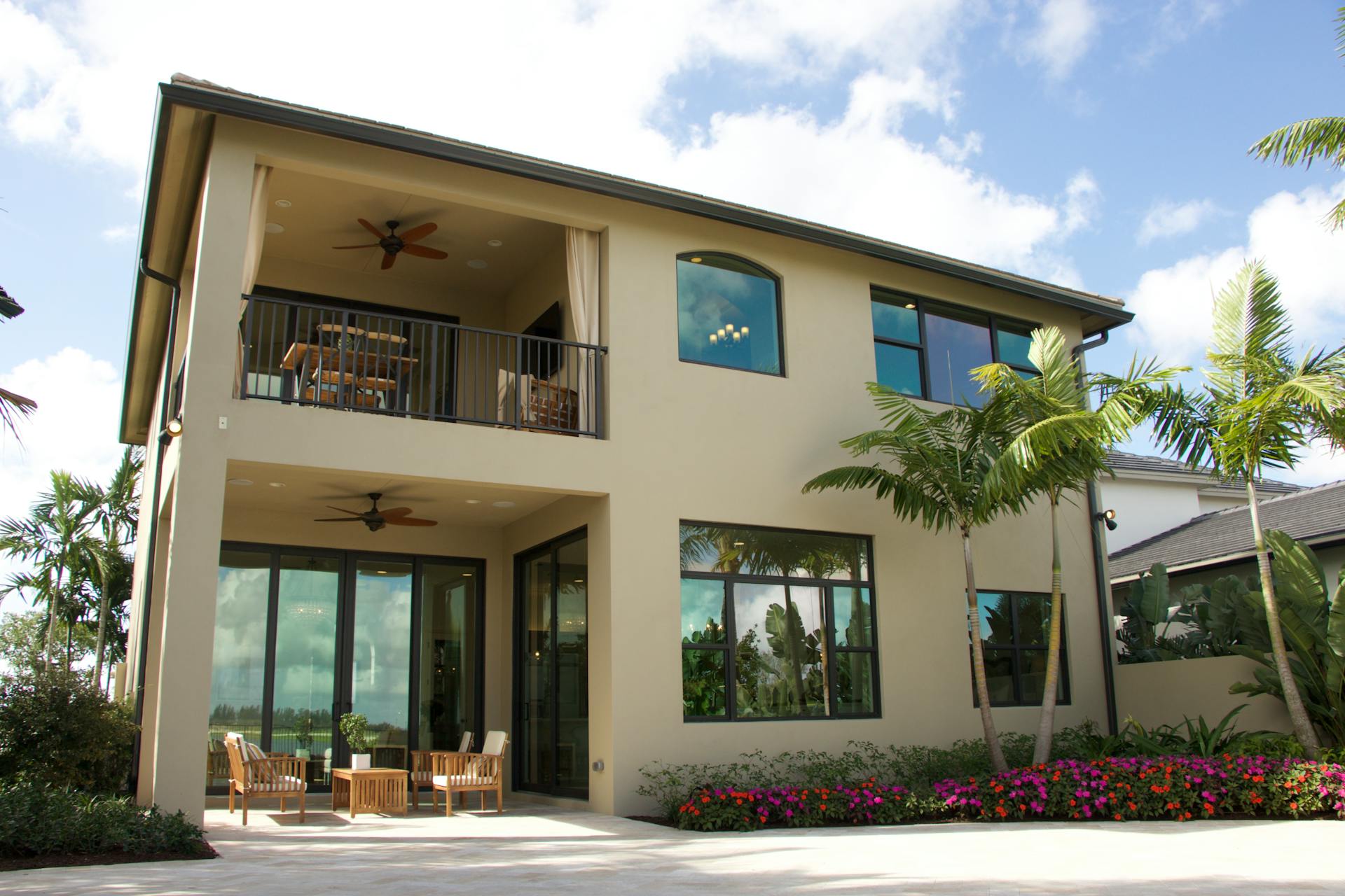 A modern two-story home in Florida with a balcony, patio, and lush garden.