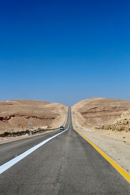 Straight road cutting through Israeli desert landscape beneath a vibrant blue sky.